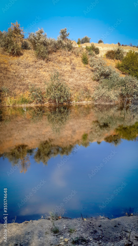 landscape river bank with yellow green trees on a summer day reflected in water