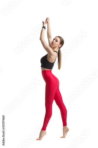 Slender athletic girl in sportswear a black top and pink leggings stands in full growth isolated on a white background.