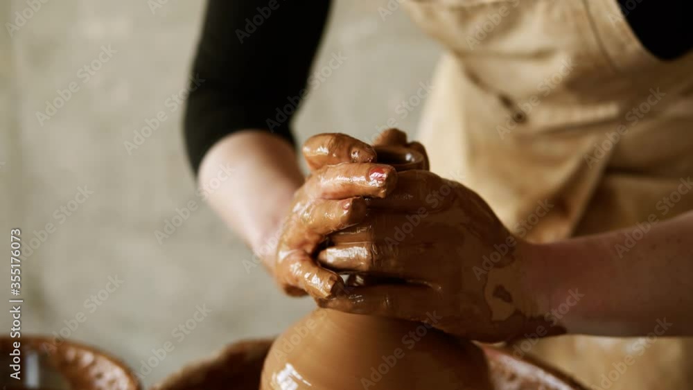 Female potter's hands with red manicure working with wet clay on a pottery wheel making a clay product in a workshop. Unrecognizable female person forming a vase, pulls up the neck Female potter's hands with red manicure working with wet clay on a pottery wheel making a clay product in a workshop. Unrecognizable female person forming a vase, pulls up the neck