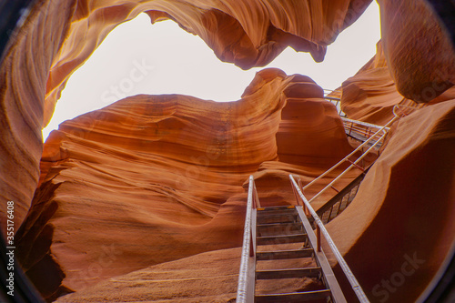 Worm's eye view of beautiful Lower Antelope canyon. A spectacular orange sandstone cave with white sky and metal stair at the entrance. Natural landscape