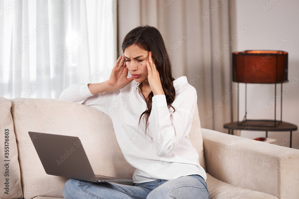 Young girl with a laptop. A young girl on the couch with a laptop holds her head. Portable electronics at home. Young girl with a laptop. A young girl on the couch with a laptop holds her head. Portable electronics at home.