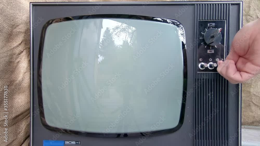 The old TV is turned on by hand. Glowing Retro TV Screen Flickers On