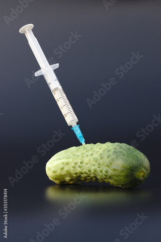 Cucumber on a black background in which the syringe gmo and nitrates are pricked. Close-up. Nitrates and genetically modified organism. photo