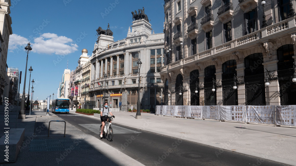 Madrid, Spain.june 02, 2020.Girl using an electric bicycle  sharing system witch mask  and a bus in alcala street, madrid.