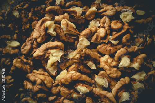 Closeup of big shelled walnuts pile. Closeup of man cracking walnuts with nutcracker in the hand.