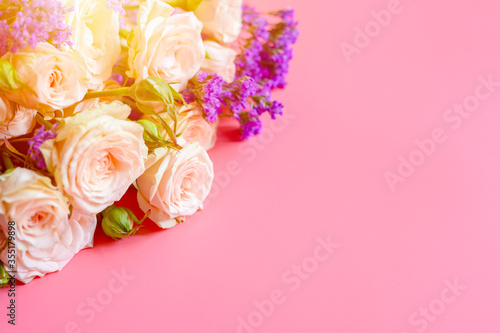 a bouquet of cream roses and bright purple flowers in full bloom on a pink background with space for text. greeting card. flare