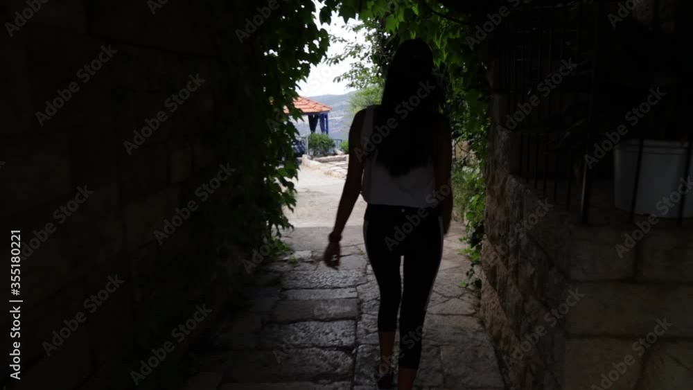 Young Caucasian Lebanese woman walking down steps inside tunnel and outside stone pathway, behind close up pan Young Caucasian Lebanese woman walking down steps inside tunnel and outside stone pathway, behind close up pan