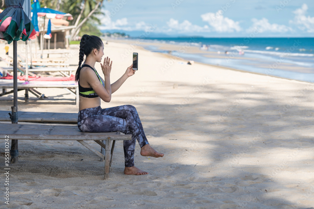 Asian woman wave hand on smartphone at beach