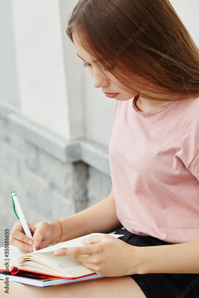 school girl writing pen in notebook on the knees. Student near university. school girl writing pen in notebook on the knees. Student near university.