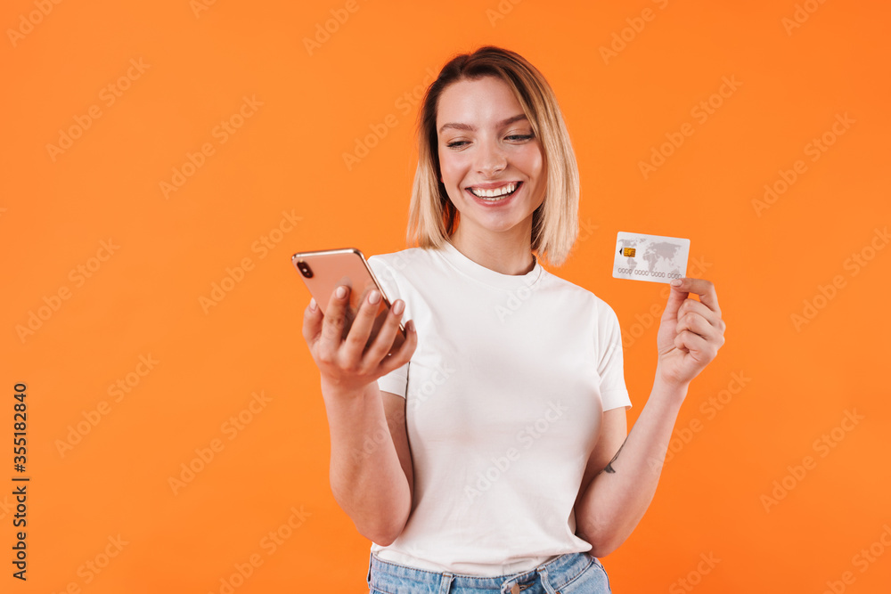 Image of happy nice woman holding credit card while using mobile phone Image of happy nice woman holding credit card while using mobile phone