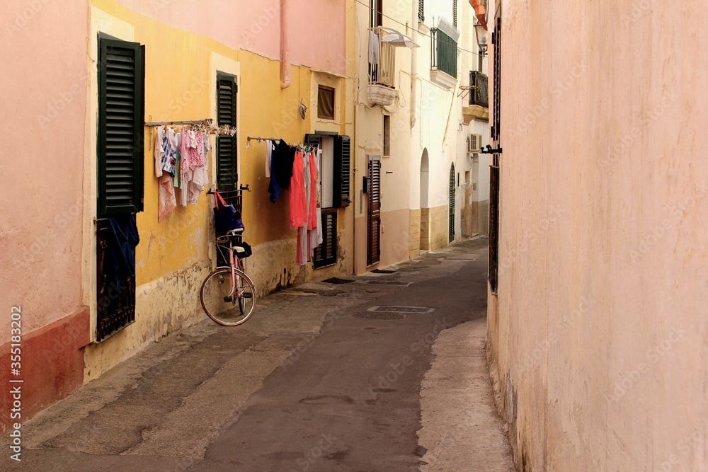 Narrow street in the old town of Gallipoli with bike, laundry drying, houses, shutters in Apulia, southern Italy