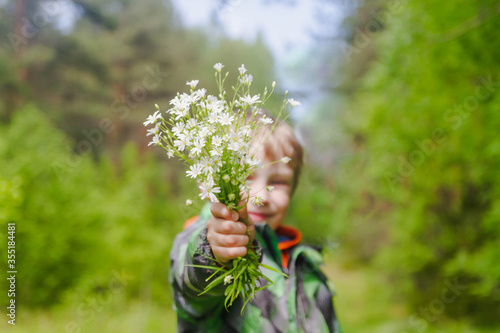 A European boy is holding a bouquet of white forest flowers.