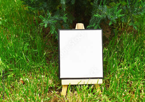 Mock up blank canvas on wooden easel in a green ivy garden, empty poster, banner, board