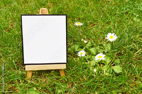 mock up empty blank canvas on wooden easel placed on green grass and daisies background, nature mock up design