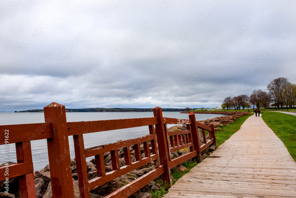 Obraz premium Redwood painted fence, lines wooden walkway winding around ocean cove in Charlottetown, Canada.