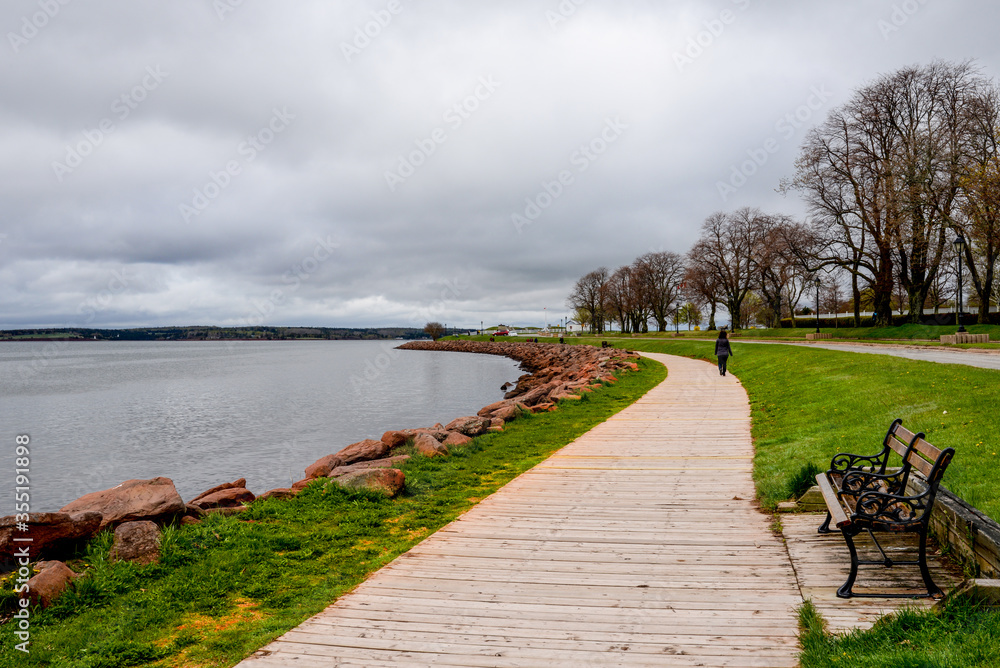 Wooden walkway edges with red rocks and flowers winds around bay in Charlottetown, Canada.