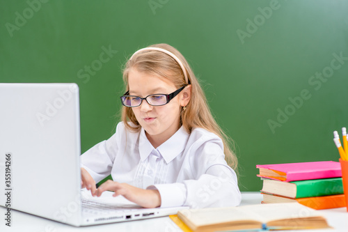 Smart young girl wearing eyeglasses uses laptop in a school