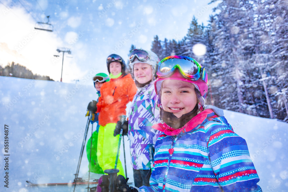 Close portrait of young girl in pink helmet in a group of ski school kids standing on the slope during winter snow