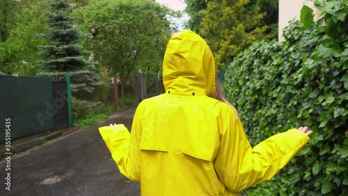 Upset young woman in yellow raincoat surprised with rain outdoors. Girl disappointed in bad summer weather and rainy days
