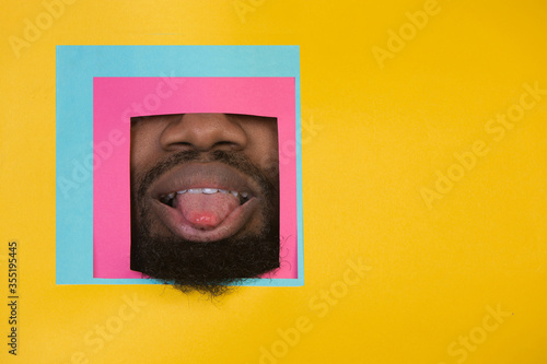 Tongue. Mouth of emotional african-american man peeks throught square in yellow background. Trendy geometrical style, copyspace. Vibrant colors. Sales, proposal, finance and business concept. Framing. © master1305