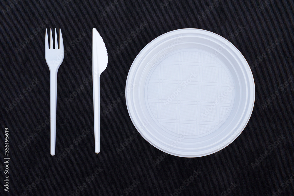 A plastic spoon and a plastic knife in a plastic plate on a black velvet background. Top view