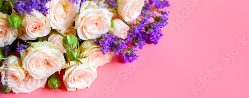 a bouquet of cream roses and bright purple flowers in full bloom on a pink background with space for text. greeting card. banner