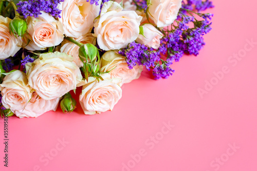 a bouquet of cream roses and bright purple flowers in full bloom on a pink background with space for text. greeting card