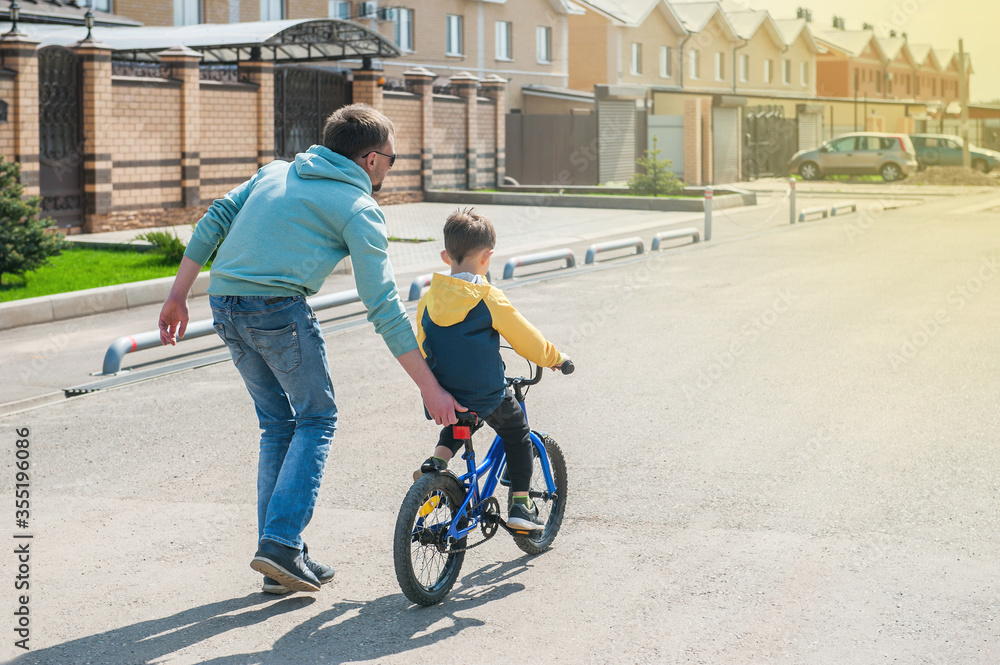 father teaches son to ride a bike. a man secures a child and holds behind the trunk of a bicycle