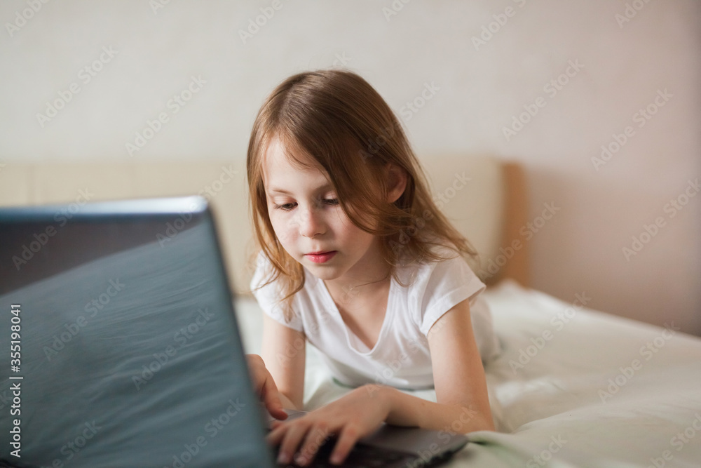 Close-up portrait of a baby girl with a laptop on the bed. The concept of digital communication, digital addiction, entertainment, distance learning online. Close-up portrait of a baby girl with a laptop on the bed. The concept of digital communication, digital addiction, entertainment, distance learning online.