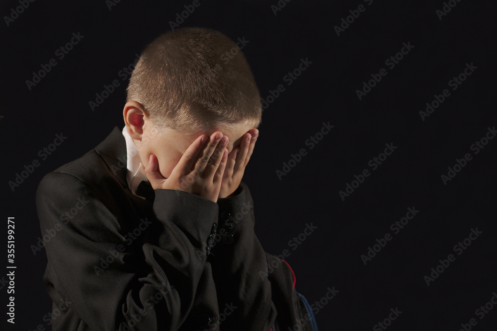 Fototapeta premium Boy student cries covering his face with his hands on a black background
