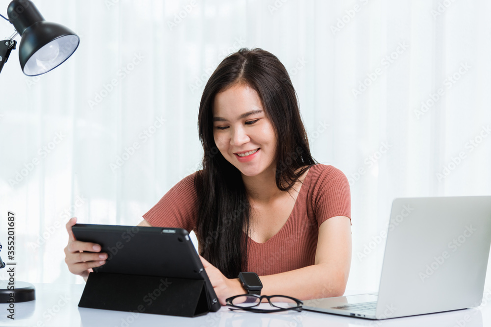 Work from home, Smiling Happy Asian business young beautiful woman sitting on desk workspace use modern smart tablet and laptop computer technology video call conferencing to team at home office Work from home, Smiling Happy Asian business young beautiful woman sitting on desk workspace use modern smart tablet and laptop computer technology video call conferencing to team at home office