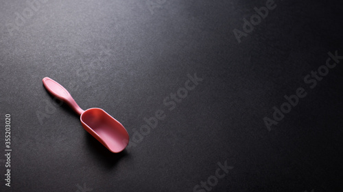 Pink plastic shovel on black texture background, office desk table from top view, copy space. 