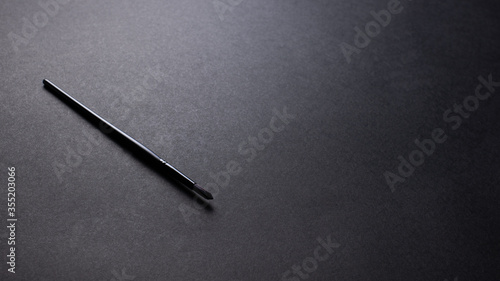 Black paintbrush for art concept on black texture background, office desk table from top view, copy space. 