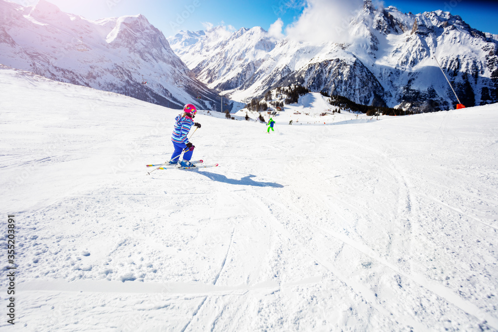 Girl in colorful ski outfit go downhill fast in the mountains