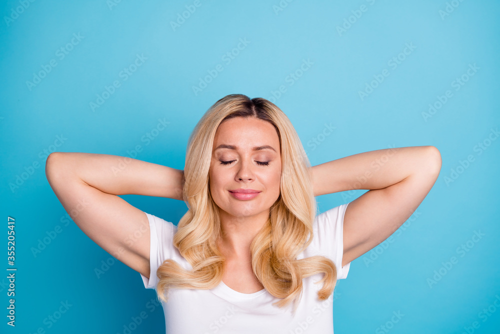 Closeup photo of attractive pretty wavy blond lady hold arms behind head eyes closed peaceful relaxing good mood wear casual white s-shirt isolated blue color background Closeup photo of attractive pretty wavy blond lady hold arms behind head eyes closed peaceful relaxing good mood wear casual white s-shirt isolated blue color background