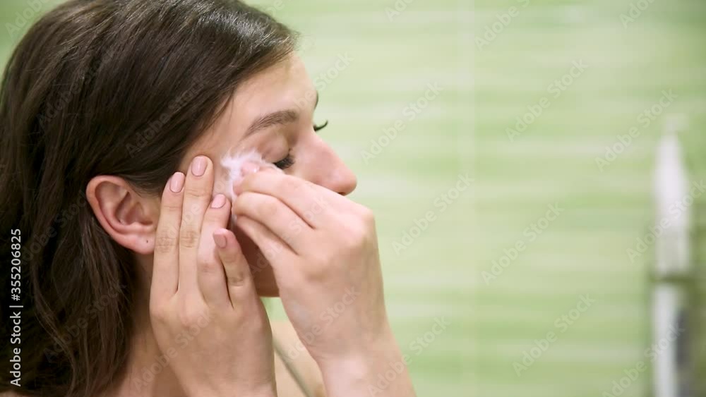 girl removes makeup using a cotton pad in a green bathroom girl removes makeup using a cotton pad in a green bathroom