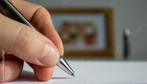 Male hand with metalic pen on beautiful white fon on warm light. Wooden picture frame and cap in the background.