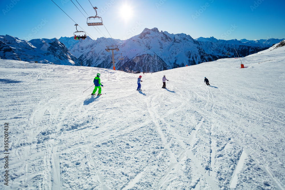 Group of kids ski downhill in Alpine slope in school formation together one after another view from behind Group of kids ski downhill in Alpine slope in school formation together one after another view from behind
