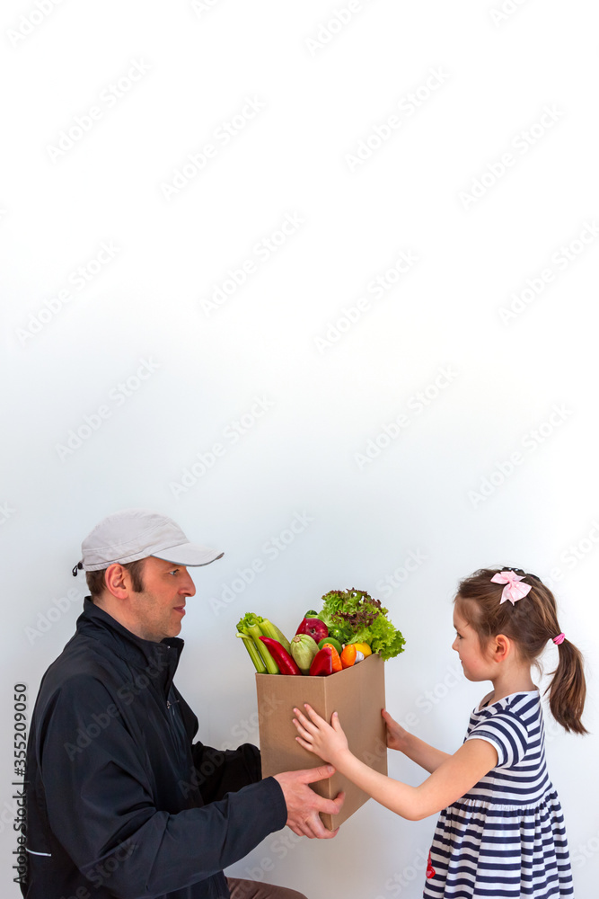 Home delivery boxes with wholesome and healthy food. The courier gives the order to the little girl. Vertical orientation. Home delivery boxes with wholesome and healthy food. The courier gives the order to the little girl. Vertical orientation.
