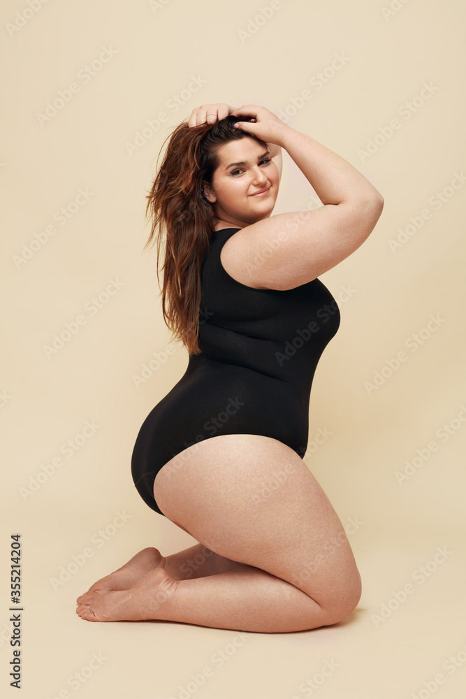 Foto Stock Plus Size Model. Big Woman In Black Bodysuit Portrait. Brunette  Touching Hair And Posing On Beige Background. Body Positive Concept. |  Adobe Stock
