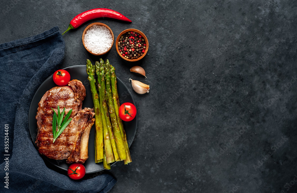 
Grilled beef steak with asparagus and spices on a black plate on a stone background with copy space for your text