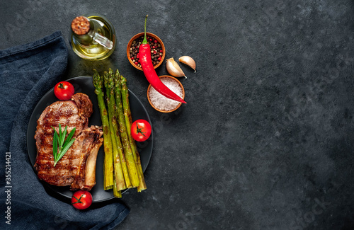  Grilled beef steak with asparagus and spices on a black plate on a stone background with copy space for your text