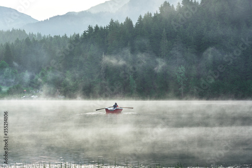 Man is rowing a boat on the foggy lake Karagol / Karagöl at sunrise. Landscape photo was taken in Savsat / Şavşat, Artvin, Karadeniz / Black Sea region of Turkey photo