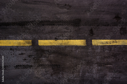 Imitation of asphalt road surface with traces of car tires and stripes of yellow markings in grunge style