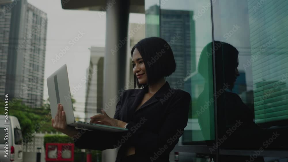 Asian young business woman standing working with laptop beside modern office. Asian young business woman standing working with laptop beside modern office.