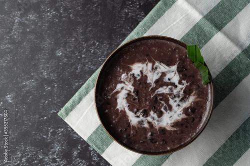 Black Glutinous Rice Porridge or Bubur Pulut Hitam in Malay with coconut milk on dark background on top napkin