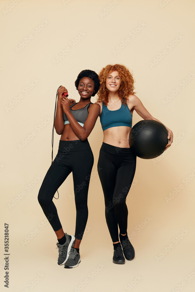 Fitness Girls. Confident African And Caucasian Women Portrait. Smiling Female Holding Exercise Equipment And Looking At Camera. Sport For Natural Beauty.