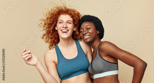 Fitness Women. Diverse Ethnic Girls Portrait. Smiling African Brunette And Caucasian Redhead Posing On Beige Background. Sport For Active Lifestyle. © puhhha