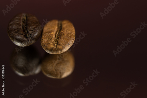Two roasted coffee beans in a row, horizontal. Extreme close up, macro photography, selective focus. Background deep red, foreground textured black with light effects. Space for copy or text.