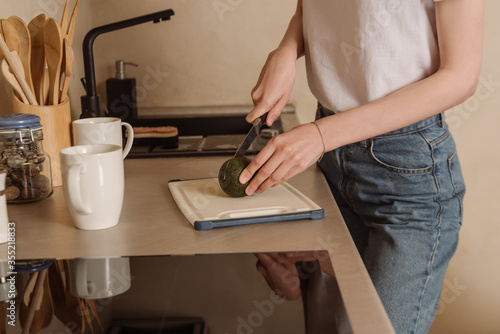 cropped view of woman cutting tasty avocado near cups